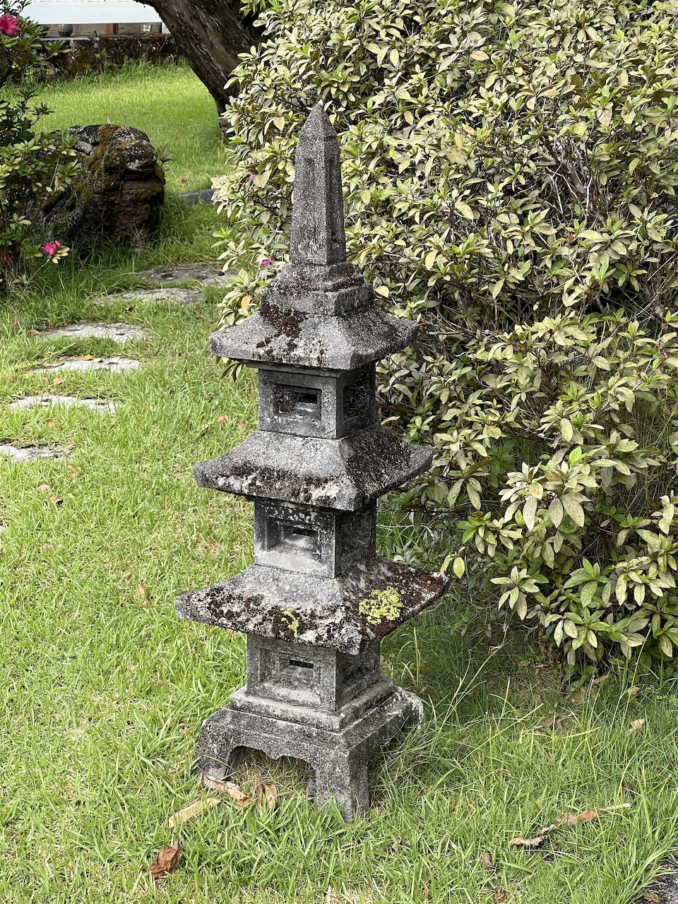 Stone pagoda lantern with multiple tiers on a green lawn in a Japanese garden