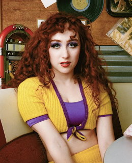 Young woman with curly red hair in yellow cardigan and purple top posing in retro vinyl record setting