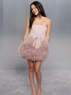 Smiling young woman in strapless pink feather dress posing against grey backdrop