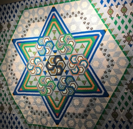 Six-pointed star quilt with nested geometric rings in blue, green, yellow and cream fabrics