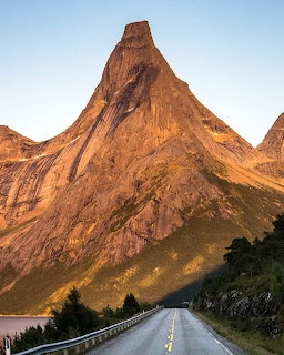 Steep granite peak of Mt Stetind Norway towering over a straight road at golden hour