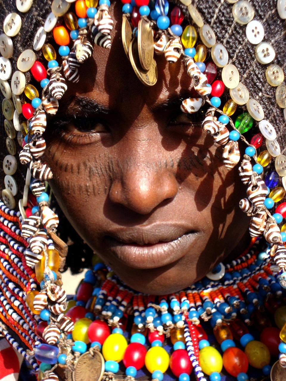 Close-up portrait of a person wearing colorful beaded jewelry, shells, and coin decorations