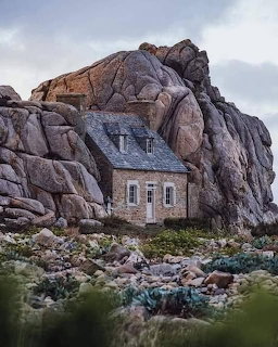 Small stone cottage beneath huge rock formations in a rugged landscape