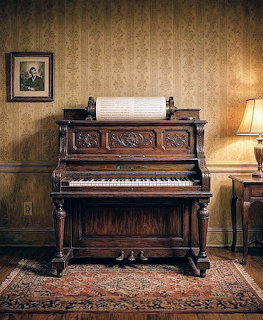Ornate vintage player piano with carved wood details in a dimly lit room with patterned wallpaper and lamp