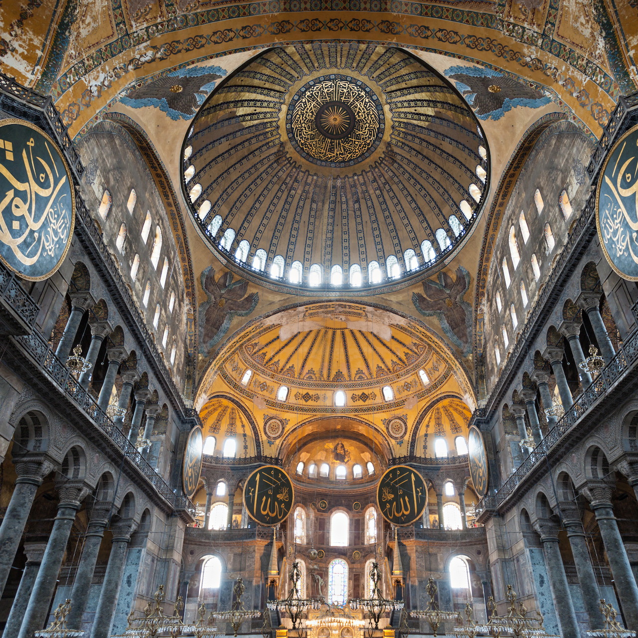 Hagia Sophia interior showing massive dome, Islamic calligraphy medallions, and sunlit arched windows
