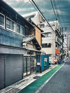 Narrow Tokyo back street with old buildings, power lines, and shuttered shops under cloudy sky