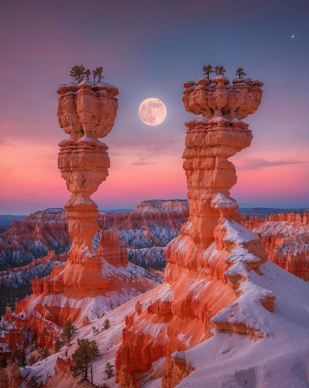 Full moon between two tall orange rock hoodoos with snow at Bryce Canyon at dusk