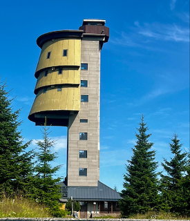 Poledník observation tower with yellow panels and cylindrical design surrounded by spruce trees