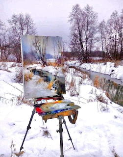 Easel with landscape painting in snowy field with trees and stream