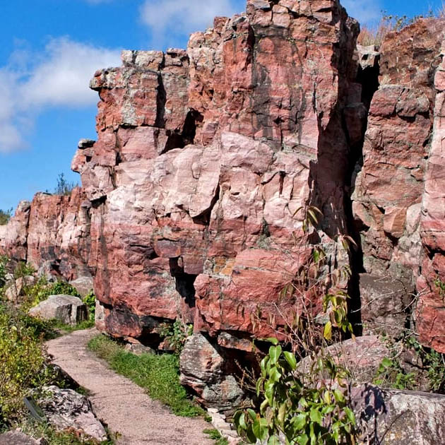Red rock cliffs beside a narrow dirt path under a blue sky