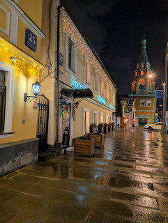 Wet cobblestone street in Moscow at night with yellow buildings, street lamps, and illuminated church tower