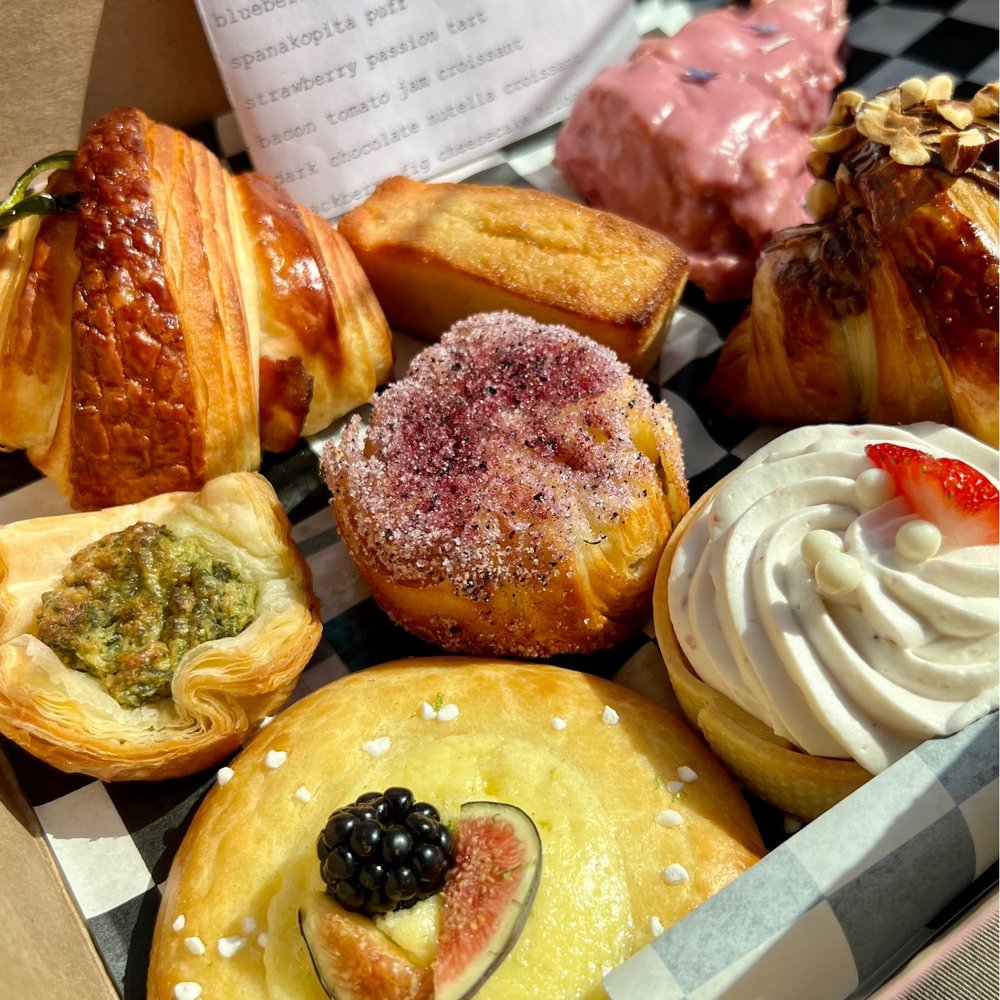 Assortment of pastries including croissants, donuts, and cream-topped desserts with decorative toppings