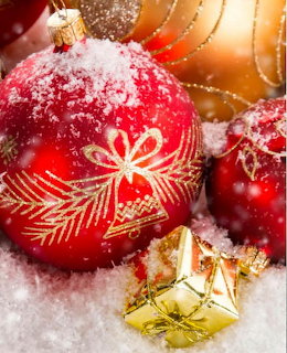 Red and gold Christmas ball ornaments with gold leaf designs lying in snow with a small gold gift box