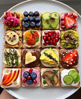 Assorted fruit-topped toast squares arranged in a 4x4 grid with blueberries, strawberries, kiwi, and other colorful toppings
