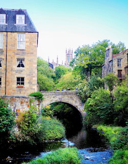 Stone bridge over river with historic buildings and greenery in Dean Village, Edinburgh