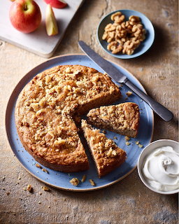 Apple crumb cake on a blue plate with sliced pieces, walnuts, apple wedges, and a bowl of cream