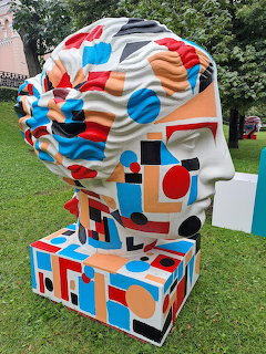 Large abstract head sculpture with colorful geometric patterns displayed on grass