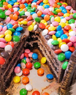 Layered chocolate cake covered with colorful candy-coated chocolates with a slice cut out