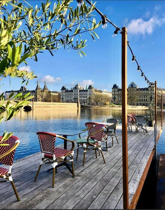 Sunny cafe terrace with colorful woven chairs on a wooden deck by a Copenhagen lake