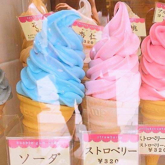 Blue and pink soft serve ice cream cones in waffle cones behind a glass display