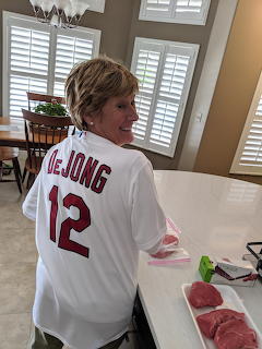 Smiling woman in white DeJong number 12 baseball jersey in a kitchen with raw meat on counter