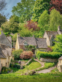 Stone cottages with steep roofs and garden paths beneath green trees in Bibury