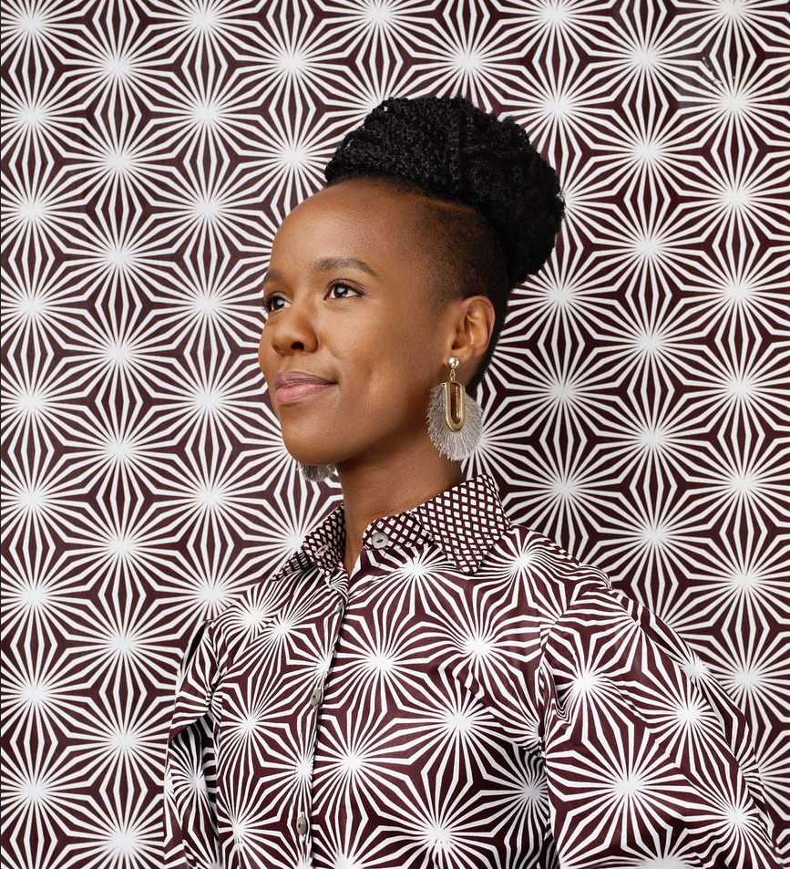 Woman with braided hair and hoop earrings posing against a black and white geometric starburst pattern background