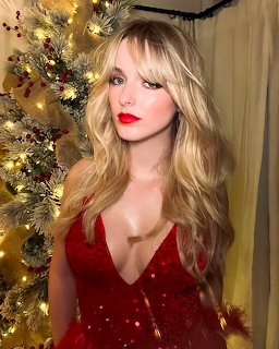 Blonde woman in red dress standing in front of a decorated Christmas tree with golden lights