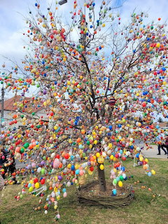 Tree covered with hundreds of colorful decorated Easter eggs hanging from branches against cloudy sky