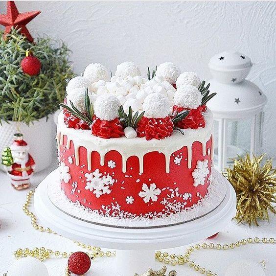 Red and white Christmas cake with coconut truffles and holiday decorations on a white table