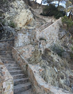 Stone steps and walls climbing a rocky hillside with sparse vegetation