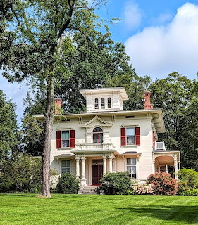 White colonial house with red shutters and columned porch on green lawn with trees