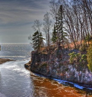 Rocky cliffs with trees along a lake shore under cloudy sky