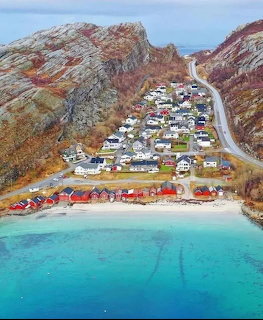 Aerial view of Norwegian coastal village with red buildings, rocky mountains, and turquoise fjord water