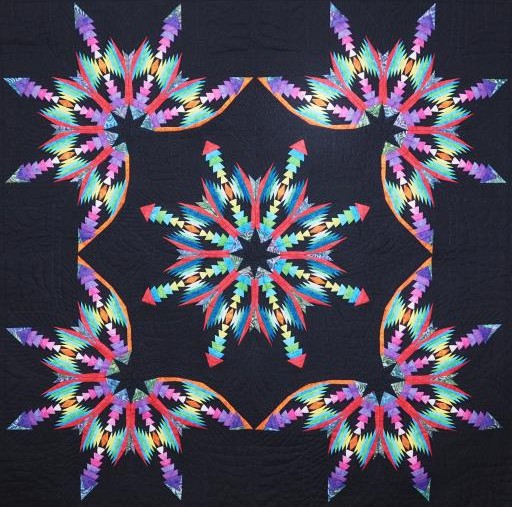 Quilt with five colorful star burst patterns radiating from center on dark blue background