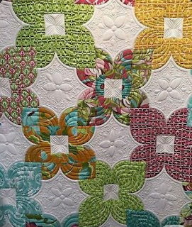 Colorful patchwork quilt with interlocking curved blocks in green, teal, pink, and yellow on white
