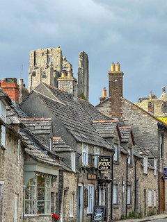 Stone cottages on village street with castle ruins in background under cloudy sky