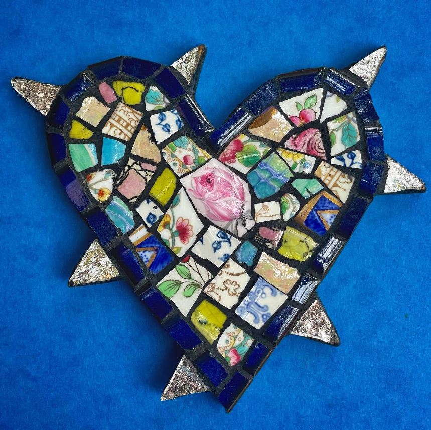 Heart-shaped mosaic with arrow made of colorful ceramic tiles and floral patterns on blue background