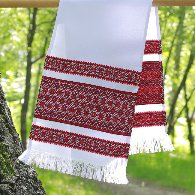 White embroidered cloth with red geometric patterns hanging on a tree outdoors