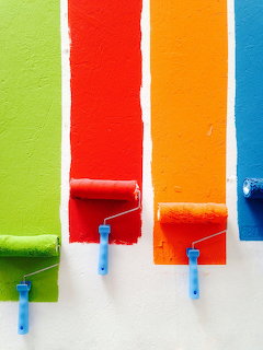 Four paint rollers with green, red, orange, and blue vertical paint stripes on a white surface