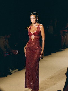 Model in a sheer sparkling dark red evening gown walking a fashion runway