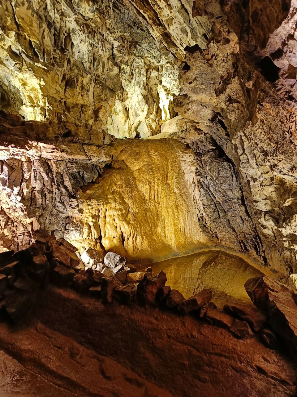 Inside a limestone cave in Wales with golden stalactites and layered rock formations lit by warm lighting