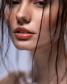 Close-up of a woman's face with wet dark hair strands and glossy lips