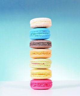 Stack of seven colorful macarons in pastel shades against a light blue background