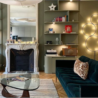 Modern living room with fireplace, shelves, glass coffee table, velvet sofa, and circular lights