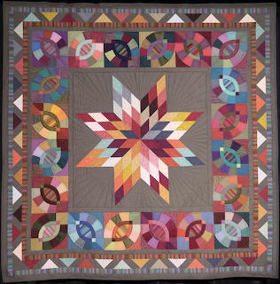 Geometric patchwork quilt with central star motif and colorful geometric border patterns on gray background