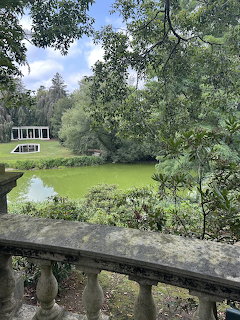 Stone balustrade overlooking a green pond with trees and a white pavilion in a garden estate