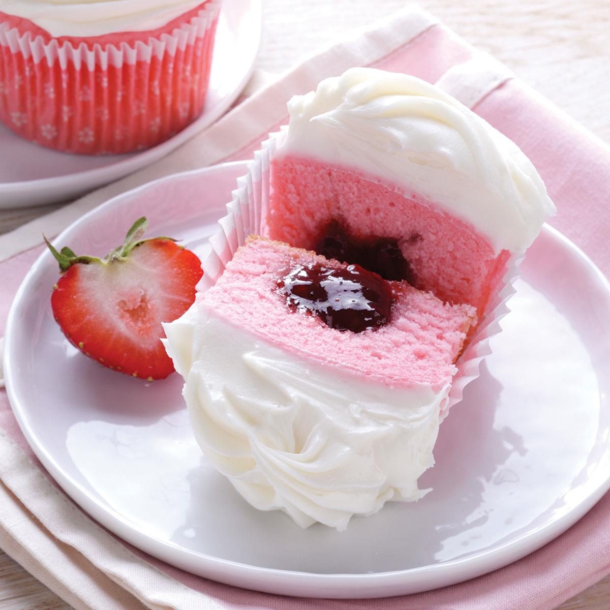 Pink cupcake with white frosting, chocolate center, and sliced strawberry on white plate