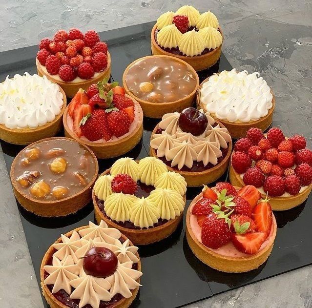 Array of decorated dessert tarts with various toppings including berries, cream, and chocolate