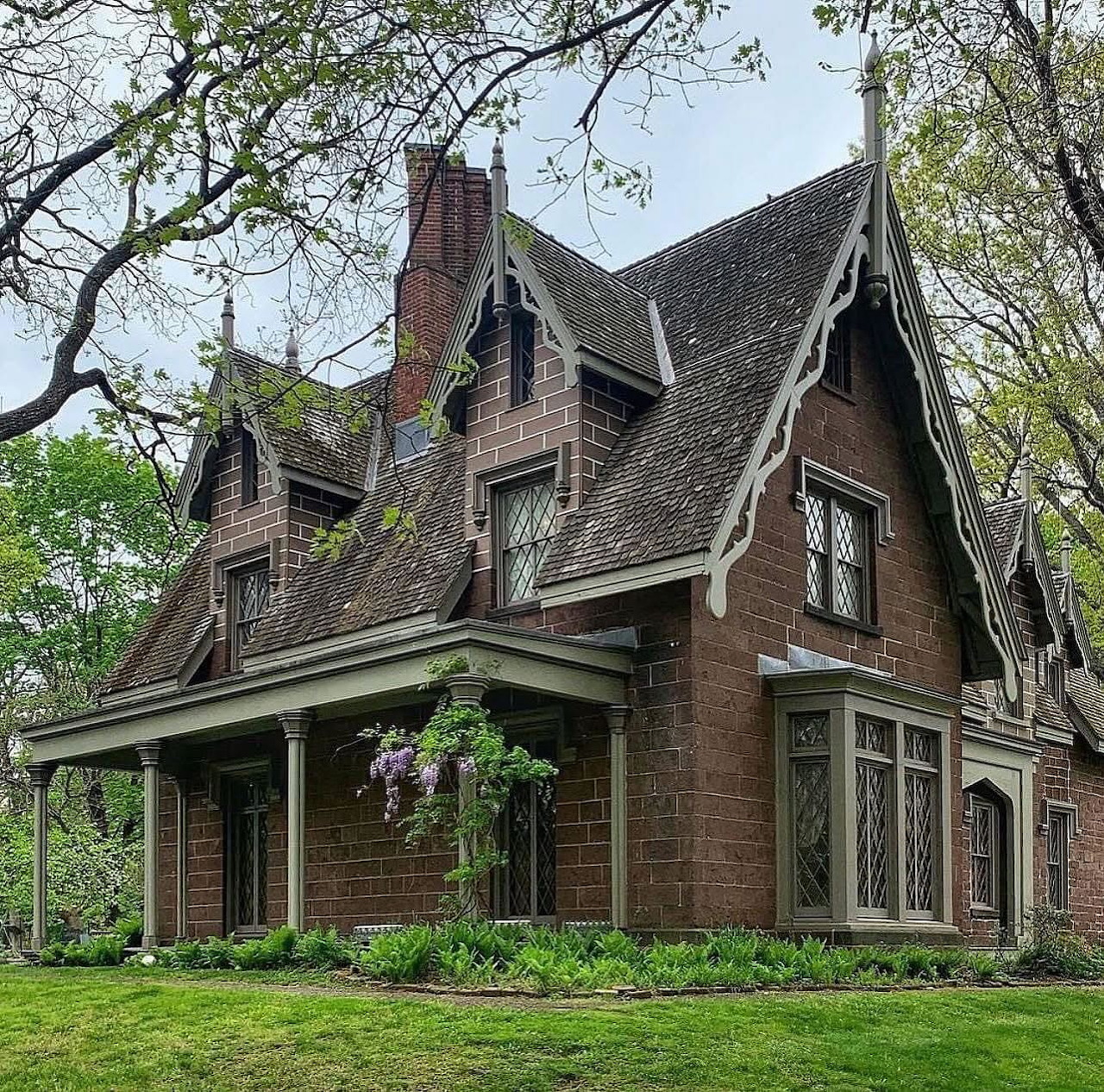 Victorian Gothic brick house with steep roof and chimneys surrounded by trees